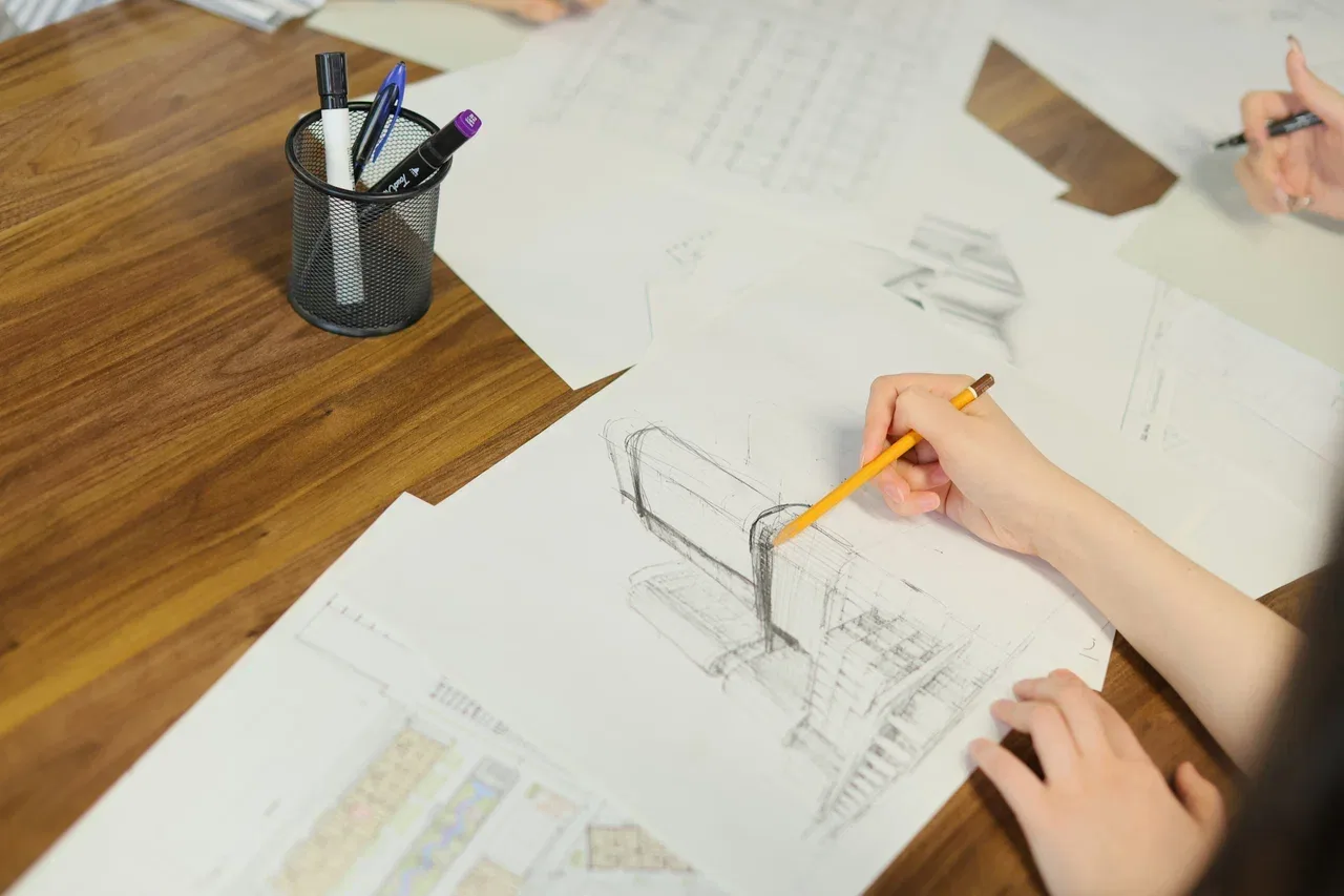 A student at SAD sketching a building in pencil, drawings and plans on the desk