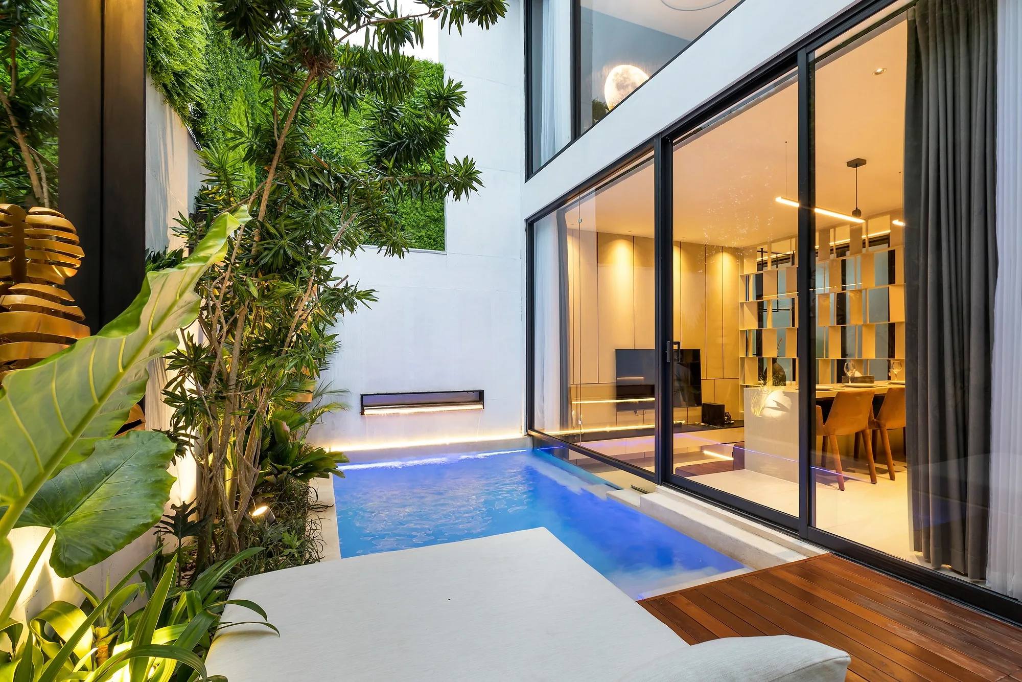 The villa courtyard in the evening: the lit pool and the glazed living room