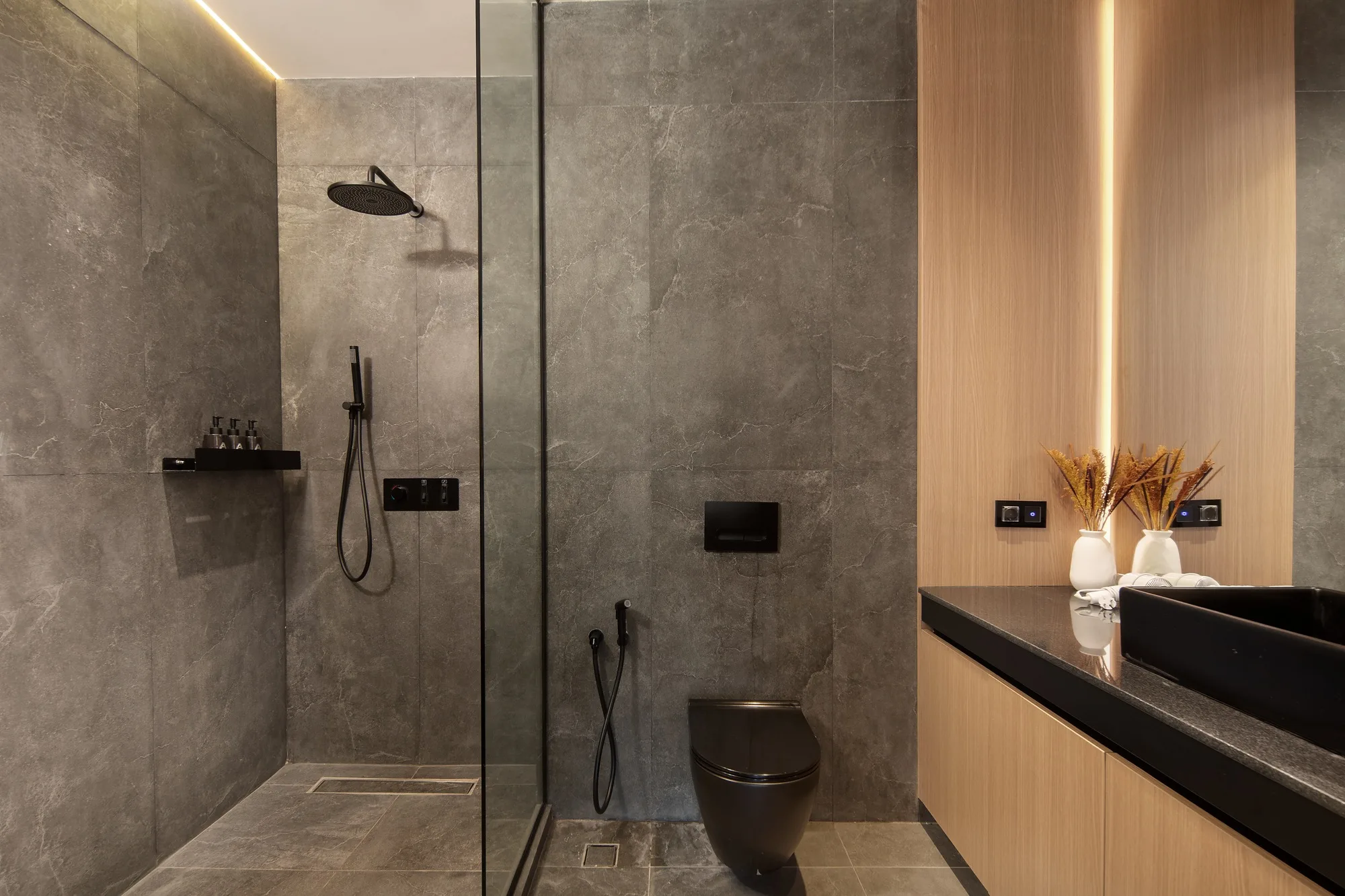 The villa bathroom: grey stone, a glazed shower and warm concealed lighting