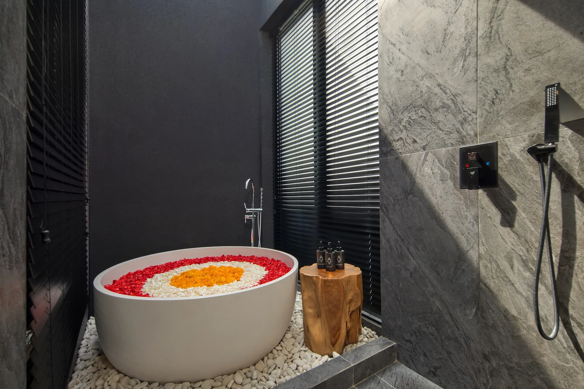 A freestanding tub with flower petals against a dark stone wall