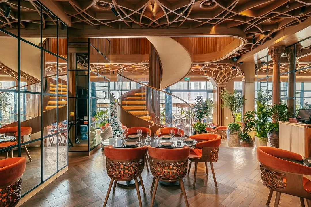 Photo of BESAR restaurant in Dubai: the dining hall with carved wooden columns and the spiral staircase — SAD studio
