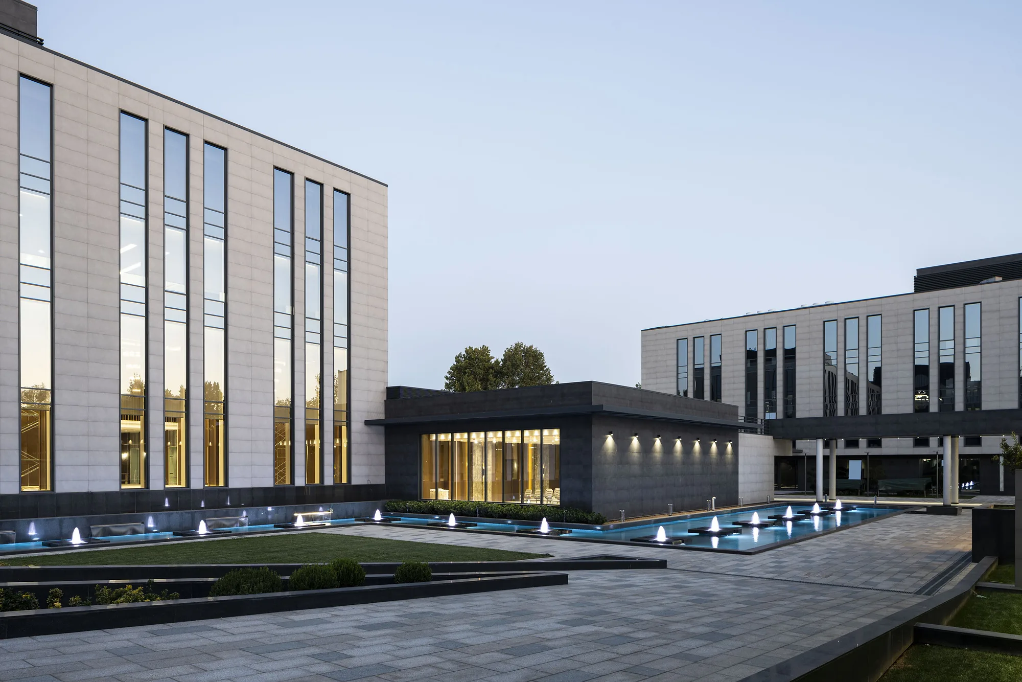 The business centre courtyard in the evening: lit fountains and a glazed entrance