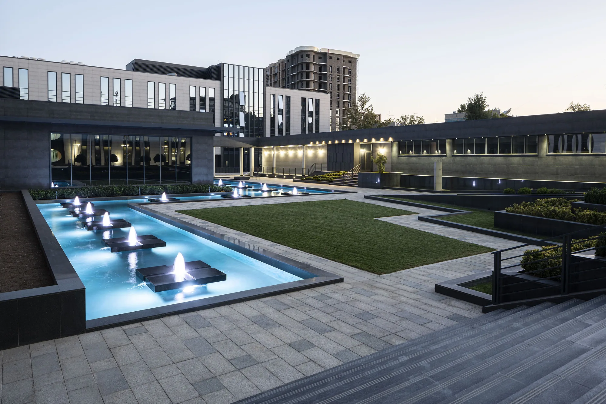 The courtyard in the evening: the lit pool and lawn between the blocks