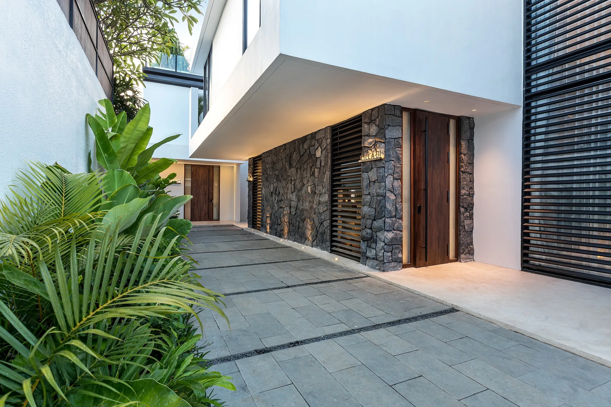 Approach to the Grey Villas on Bali: white cantilevered volumes, dark stone walls and timber doors