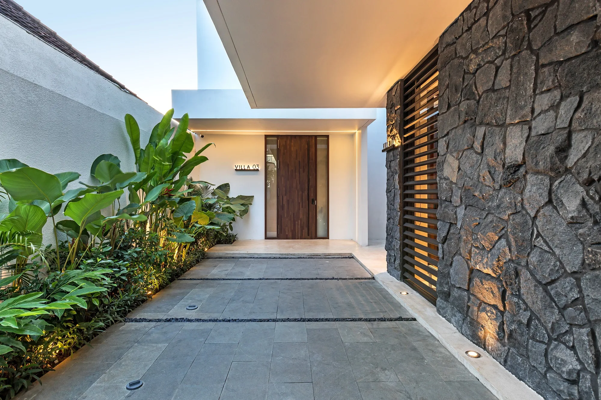 Villa entrance: a timber door between a dark stone wall and a louvred screen