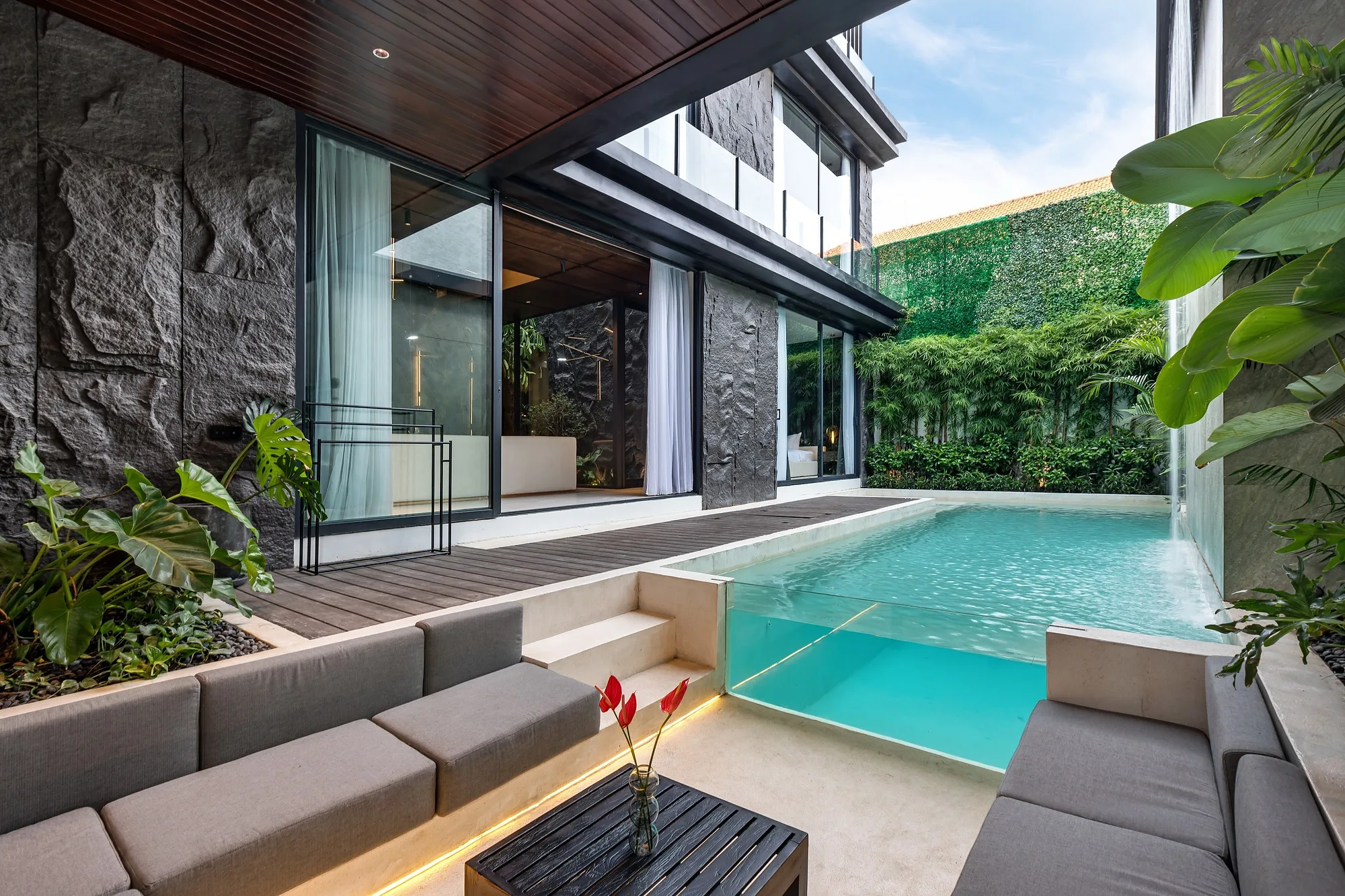 Villa courtyard: full-height living room glazing, the pool and a seating area under the canopy