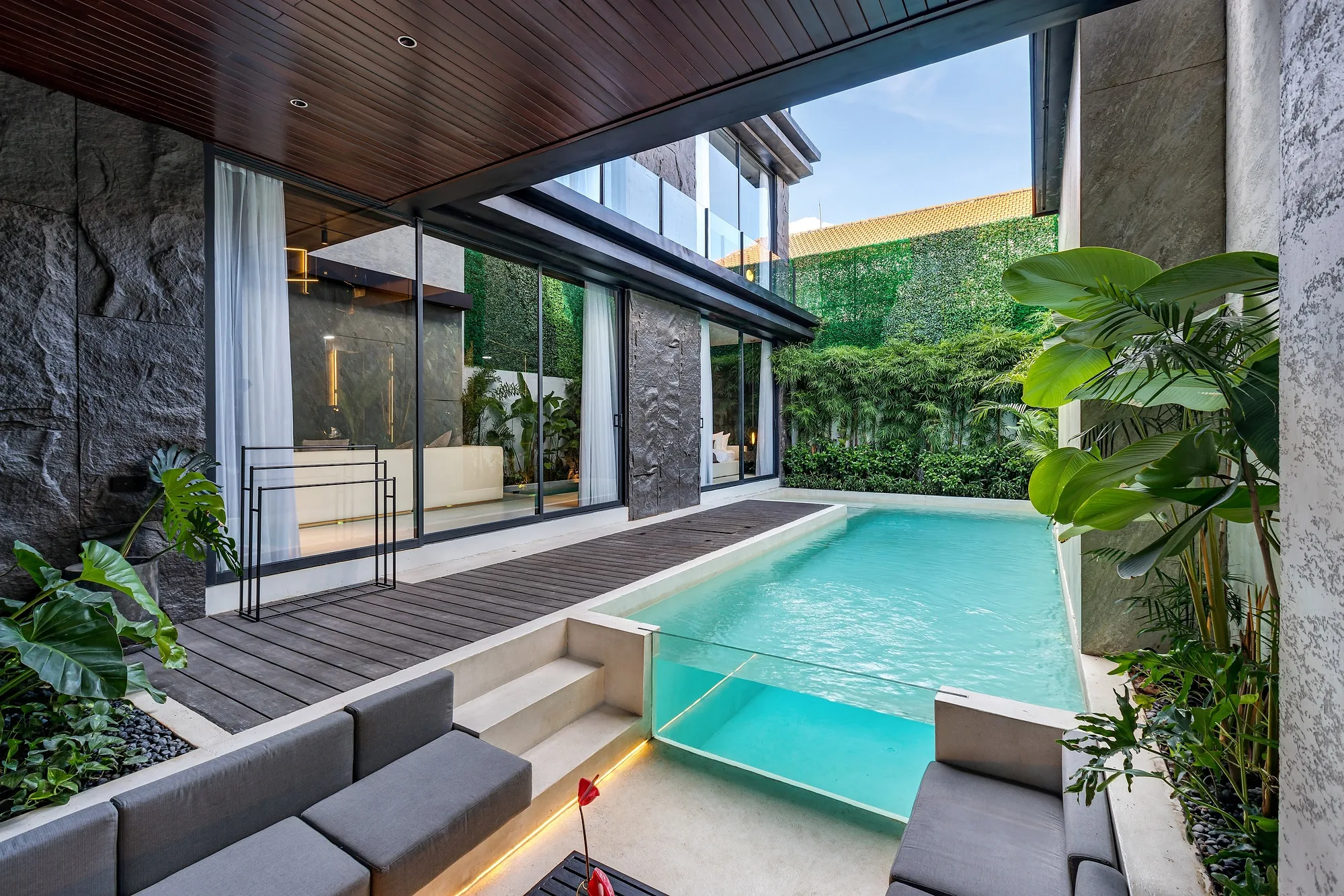 The villa pool with a glass panel in its wall against the dark stone