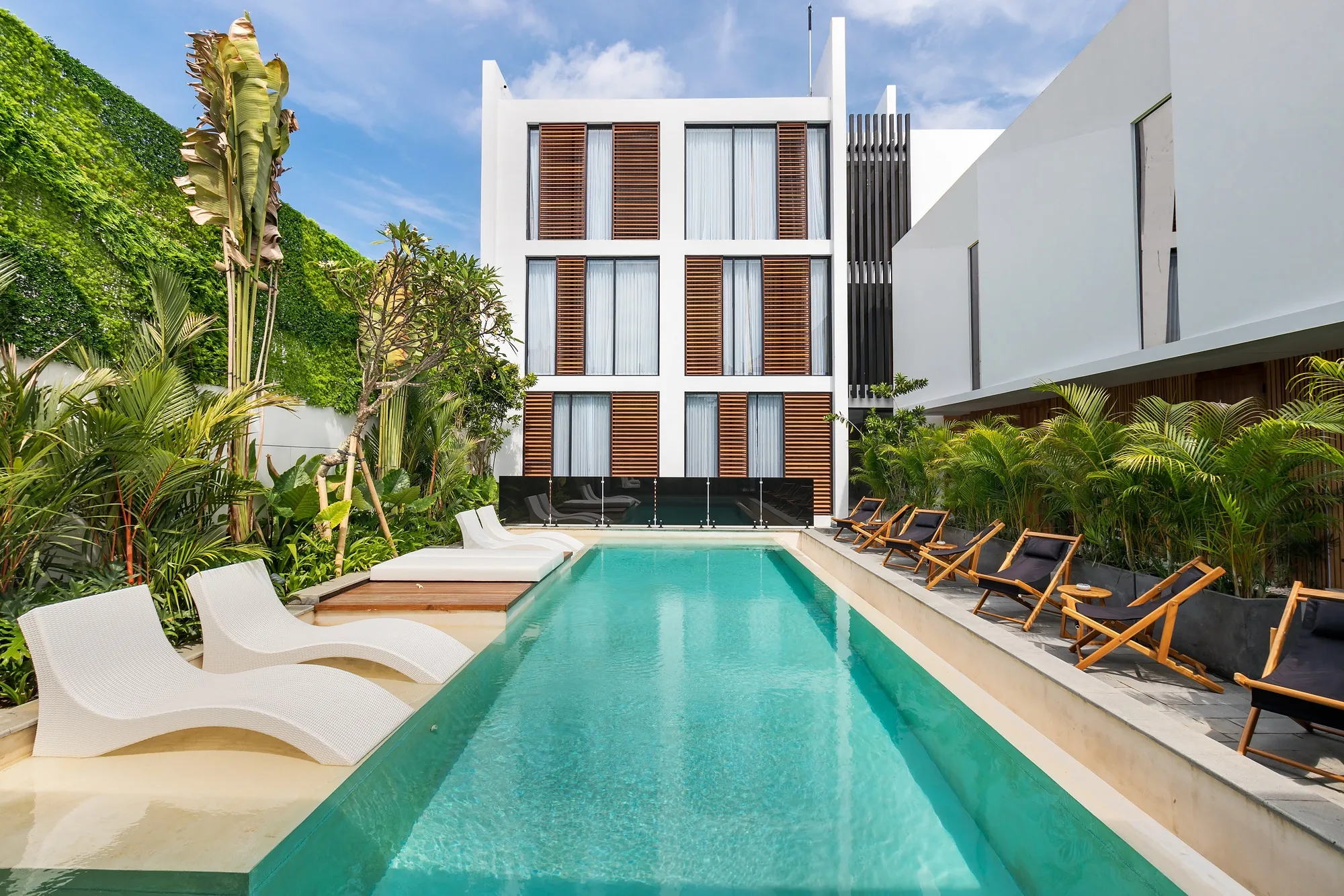 The complex facade from the pool side, loungers along the water