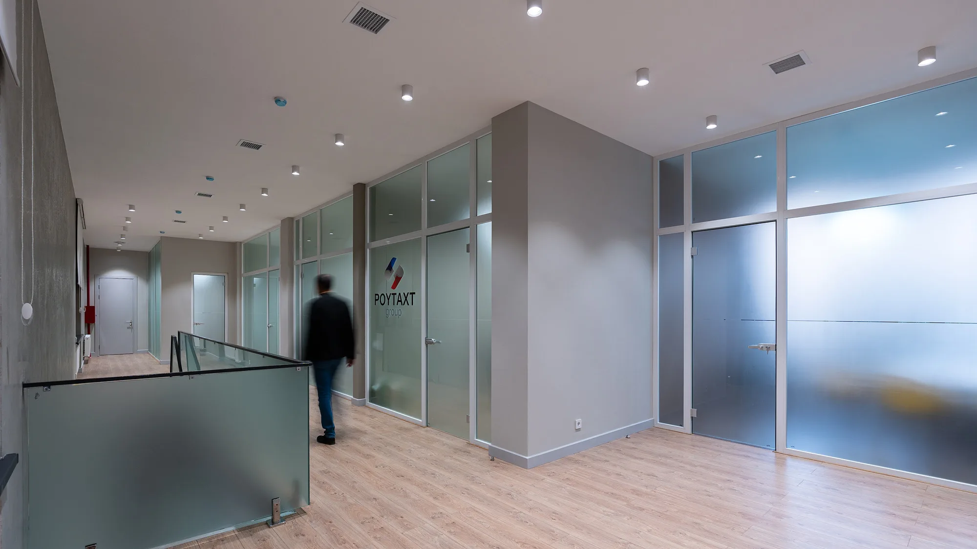 Circulation zone of the Poytaxt Group office in Tashkent: frosted glass office partitions and the logo on the wall — SAD studio