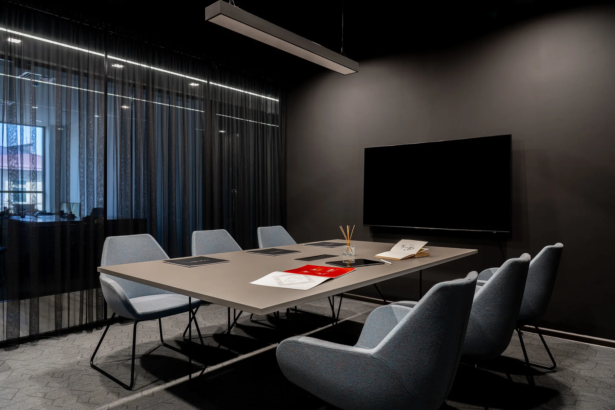 Meeting room of SAD studio: an eight-seat table, a screen on the dark wall and heavy curtains — SAD studio