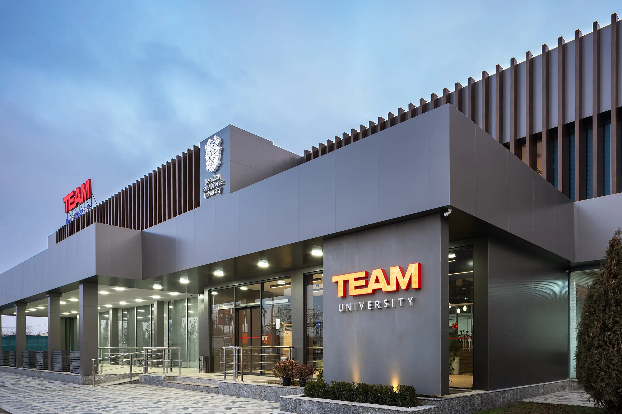 Entrance to TEAM University in Tashkent: the lit portal with the university name and the crest on the facade — SAD studio