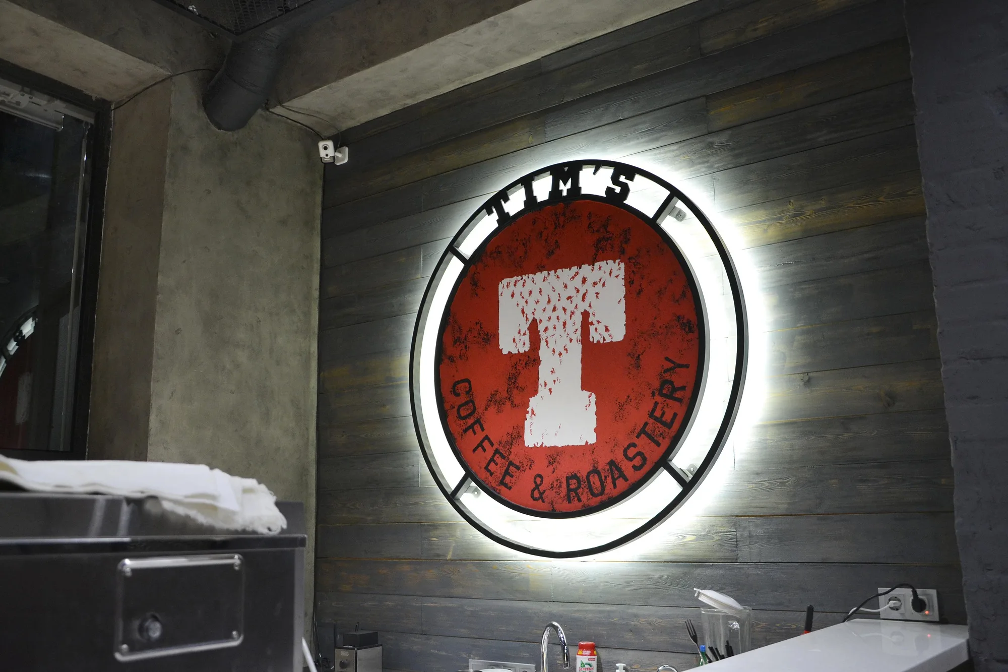 TIM'S Coffee & Roastery in Tashkent: the lit TIM'S logo on a timber wall — SAD studio