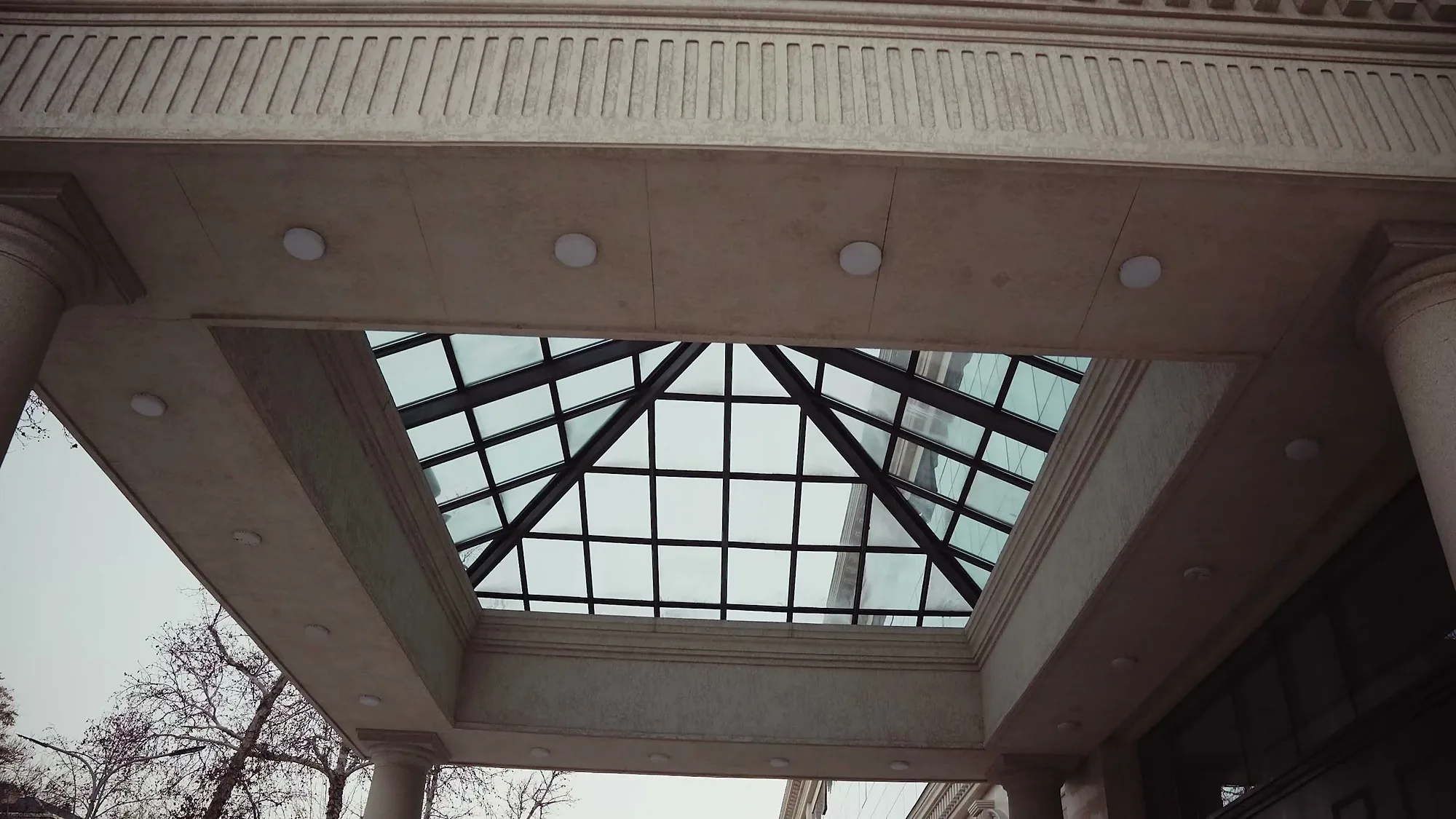 The glazed entrance canopy of Trast Bank in Tashkent from below: a glass pyramid set into the slab — SAD studio